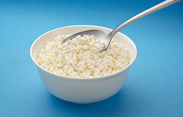 Bowl of cottage cheese with spoon on blue background