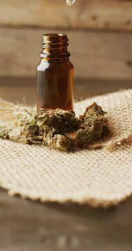 Vertical video of marijuana buds and bottle of cbd extract on wooden background