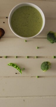 Vertical video of cream peas soup and broccoli lying on wooden surface