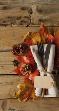 Vertical video of cutlery, cloth, autumn leaves and cones lying on wooden surface