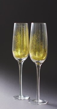 Vertical video of gold glitter in two champagne flute glasses