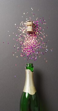Vertical video of champagne bottle and exploding cork with colourful pink and gold glitter