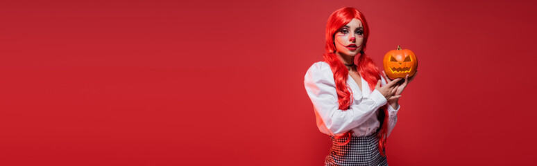 woman with colored hair and clown makeup standing with carved pumpkin isolated on red, banner.