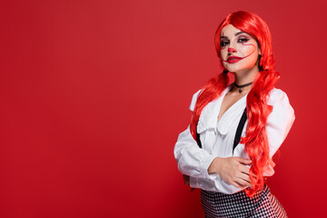 woman with bright colored hair and halloween makeup posing with crossed arms isolated on red.