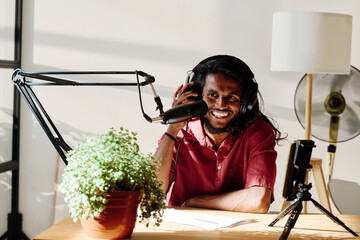 Young cheerful man in headphones speculating about topical subject while talking in microphone...