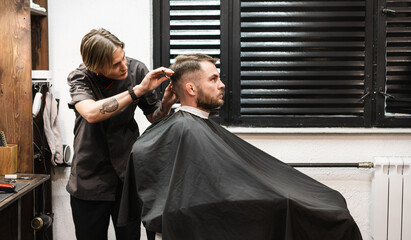 Young stylish woman barber working in the barbershop serving male customers, barber occupation.