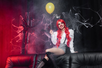 happy woman with clown makeup and yellow balloon looking at camera on dark background with spiderweb.