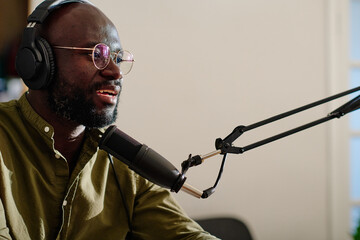 Young modern male host in headphones sitting in front of microphone and speculating about topical...