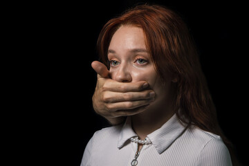 A man's hand covers the girl's mouth on a black background. The concept of domestic violence and...