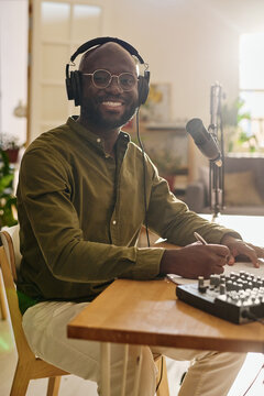 Young successful African American male host in headphones looking at camera while sitting by desk and making plan of speculation
