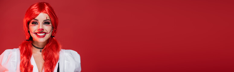 laughing woman with colored hair and halloween makeup laughing at camera isolated on red, banner.