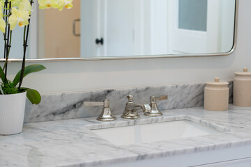 Modern bathroom details of gray marble counter with white cabinets, large mirror and yellow orchid...