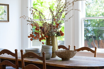 Country style dining room detail of natural wood table with chairs and center dried floral...