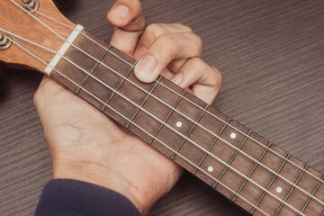 Fototapeta na wymiar ukulele in close up with hand placing chords. The chord is C. Portable string instrument. Music creation concept. Isolated wooden background.