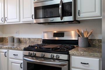 Modern kitchen details of gas stove with microwave above, stone counter tops and white cabinets.