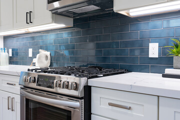 Modern kitchen details of white marble counter, gas stove, and blue tile backsplash.