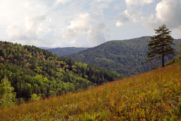 Autumn landscape, forested mountains, cloudy sky.