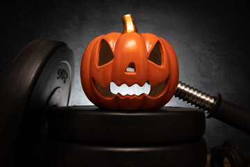Ceramic Halloween pumpkin on a barbell weight plates. Healthy gym fitness lifestyle autumn or fall...