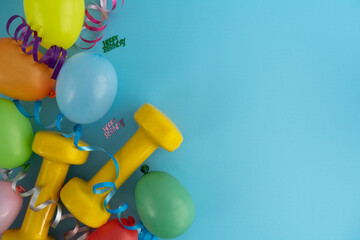 Two yellow dumbbells, colorful balloons and ribbons. Gym exercise equipment as a gift for birthday...