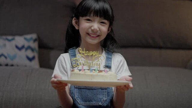 Asian happy family of little girl showing cake. Celebrate birthday anniversary party on table at night in living room. Kid girl having happiness lifestyle.
