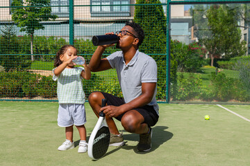 Father and daughter drinking water on a paddle tennis court