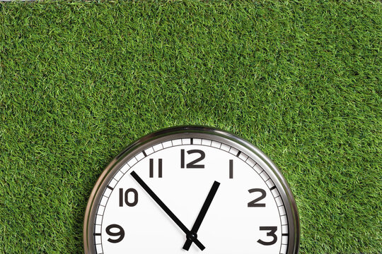 White plain analogue wall clock on green turf grass background. Five to one o'clock. copy space, game time management concept. opening or closing hours. Ecological sustainable business banner