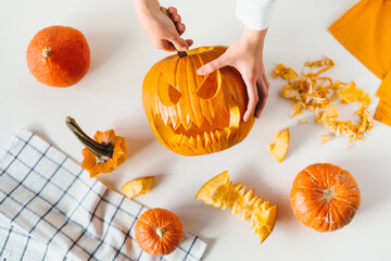 Happy halloween, decoration and holidays concept. Young woman hands with knife carving pumpkin or jack-o-lantern on white table background at home. Close-up, top view, flat lay