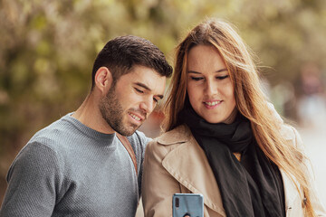 couple in autumn looking at mobile phone in the street outdoors