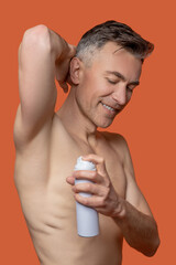 A mid aged man with a deo spray looking cheerful after shower
