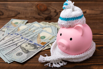 Savings concept. Piggy bank and money on a brown wooden table. Piggy bank in a warm winter hat and scarf, heat saving. Saving heating concept.Place for text. Copy space