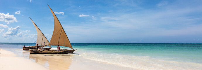 Sansibar, Dhows an einem Strand an der Küste der Insel. Boote im türkisfarbenes Ozean und blauer Himmel in Tansania, Panorama. - obrazy, fototapety, plakaty