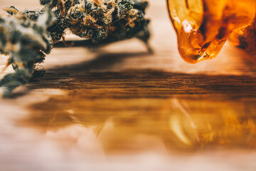 Cannabis flowers on the oak piece of wood  background with small and old apothecary bottle with marijuana oil inside.
