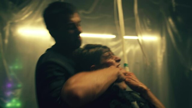 Bandit or criminal fighting with police officer and strangling him with wires in dim basement with LED lamps. Scene from action movie