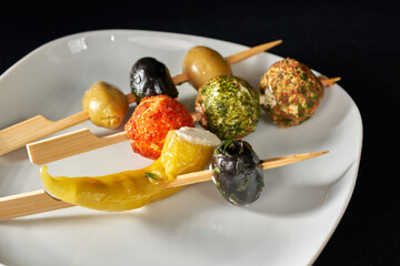 Finger food sticks with olives and stuffed pepperoni on white plate.