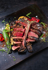 Traditional barbecue dry aged wagyu porterhouse beef steak bistecca alla Fiorentina with grilled vegetable and spice sliced and served as close-up on an old rustic board