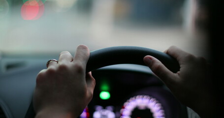Driver point of view, hands holding steering wheel driving in evening in urban city