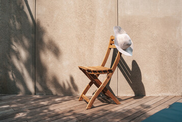 Hat hanging on the wooden chair standing at the terrace. Summer mood background with copy space.