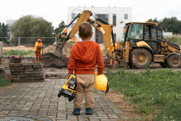Child with excavator near construction site, dreams to be an engineer. Little builder. Education, and imagination, purposefulness concept - 530416446