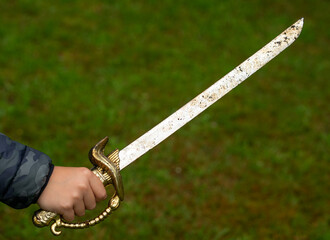 A child's hand holds a pirate saber. A child's hand with a pirate's golden saber. Sword fighting.