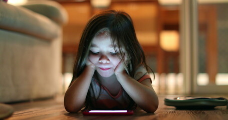 Child girl lying on hardwood floor at night watching cellphone screen