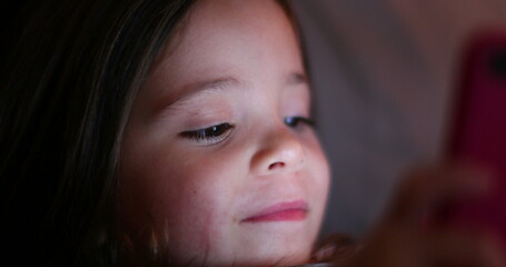 Child girl looking at cellphone screen device. Little girl using smartphone. Glowing light face