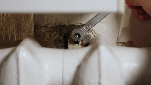 Hands is screwing bolt into old bracket to strengthen heating radiator.