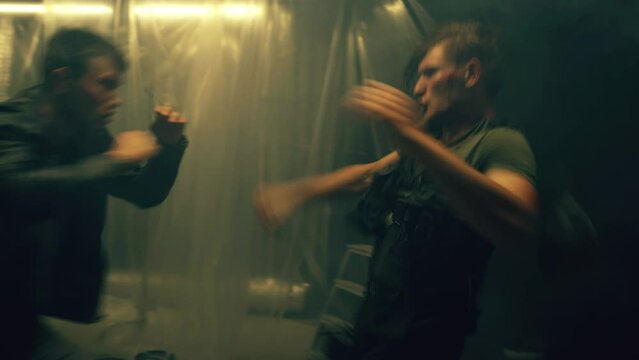Male criminal or gangster and policeman hitting each other in close fight in dark and dusty basement. Scene from action movie
