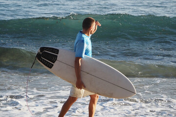 Surfer with surfboard on shore, checking out waves.