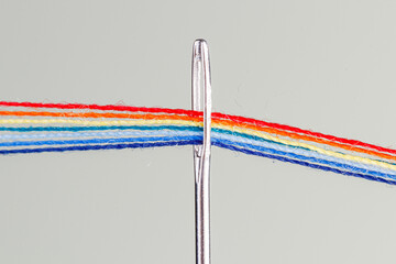 multi-colored threads for sewing in the form of a rainbow pass through an antique needle on a white background