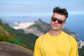 Handsome young man in sunglasses smiles and stands on a mountain against the backdrop of mountains...