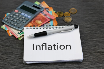 Das Wort Inflation auf einem Notizblock mit Taschenrechner und Euro Banknoten.	