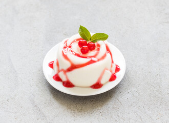 Vanilla cream pudding Panna Cotta in the shape of a rose, with red currant sauce, on a plate. Light grey background. Top view