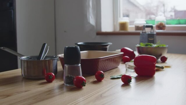Food ingredients and kitchen stuff are lying on table, fresh vegetables, greens, spices, saucepan, kitchen tools, cherry tomatoes, process of preparing tasty meal, Foreground, Slow motion.