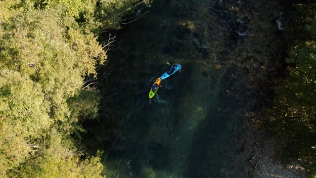 Two kayaks, blue and yellow, whitewater kayaking traversing down a series of rapids, aerial shot.